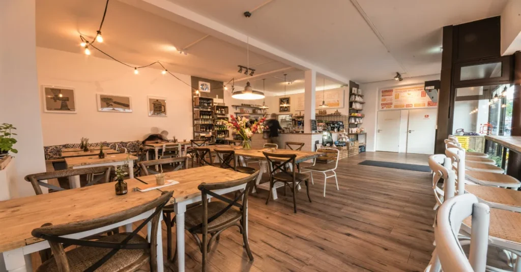 A warm, cozy, and beautifully lit modern coffee shop interior with wooden tables, chairs, and string lighting.