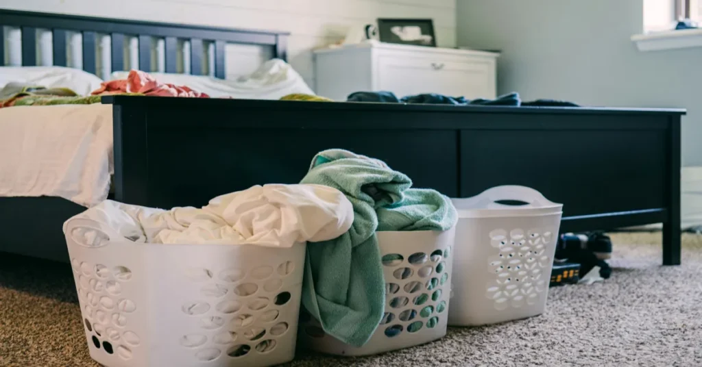 Piles of dirty clothes and laundry baskets inside a small bedroom, showing the daily hassle of managing laundry without a home washing machine.