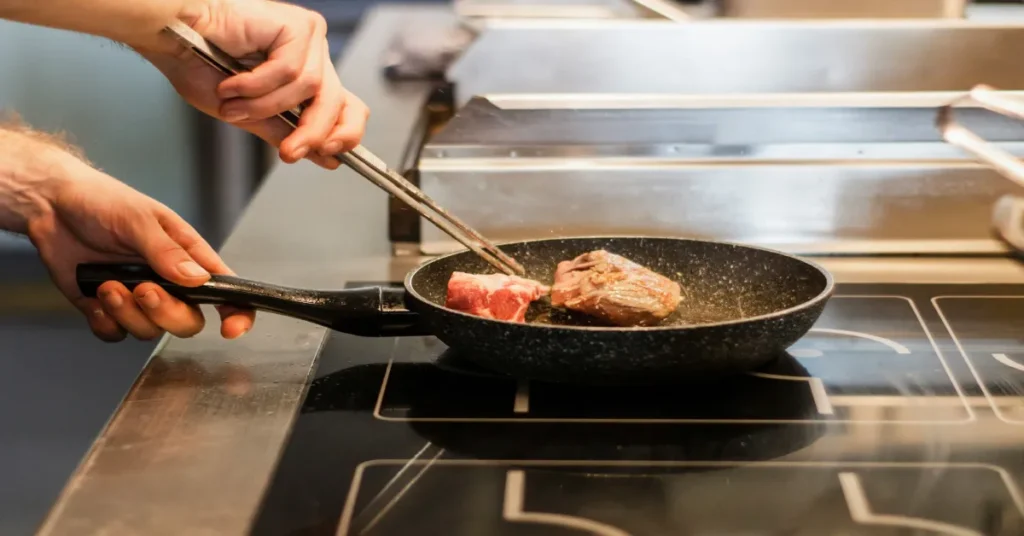 Person cooking meat in a skillet on a portable induction burner